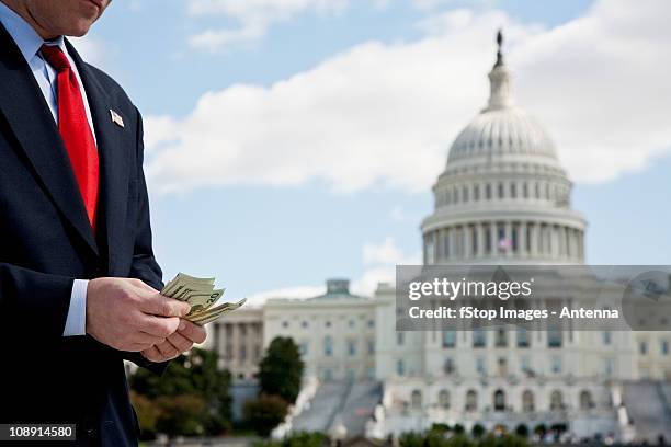 a politician counting money in front of the us capitol building - amerikanischer kongress stock-fotos und bilder