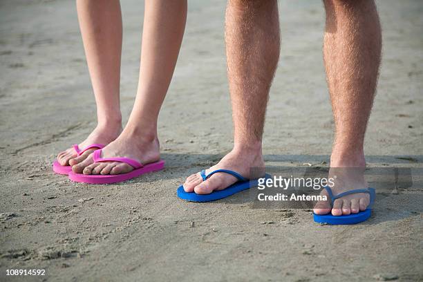 a young couple wearing flip-flops at the beach, low section - flip flop stock-fotos und bilder