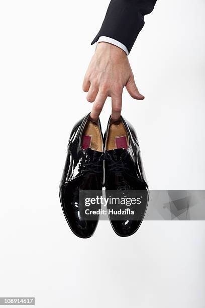 a man holding a pair of patent leather dress shoes, focus on hand - dress shoe imagens e fotografias de stock