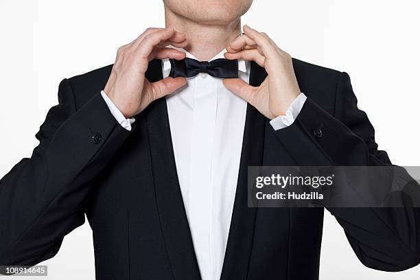 a man wearing a tuxedo adjusting his bow tie - smoking fotografías e imágenes de stock