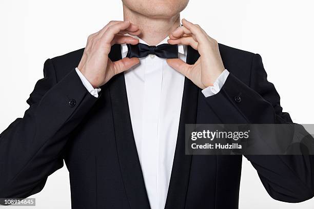 a man wearing a tuxedo adjusting his bow tie - tuxedo stock pictures, royalty-free photos & images