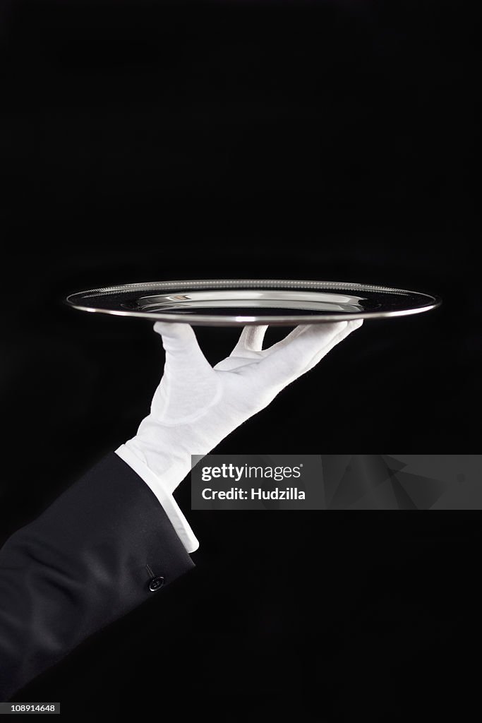 A butler presenting an empty silver tray, focus on hand