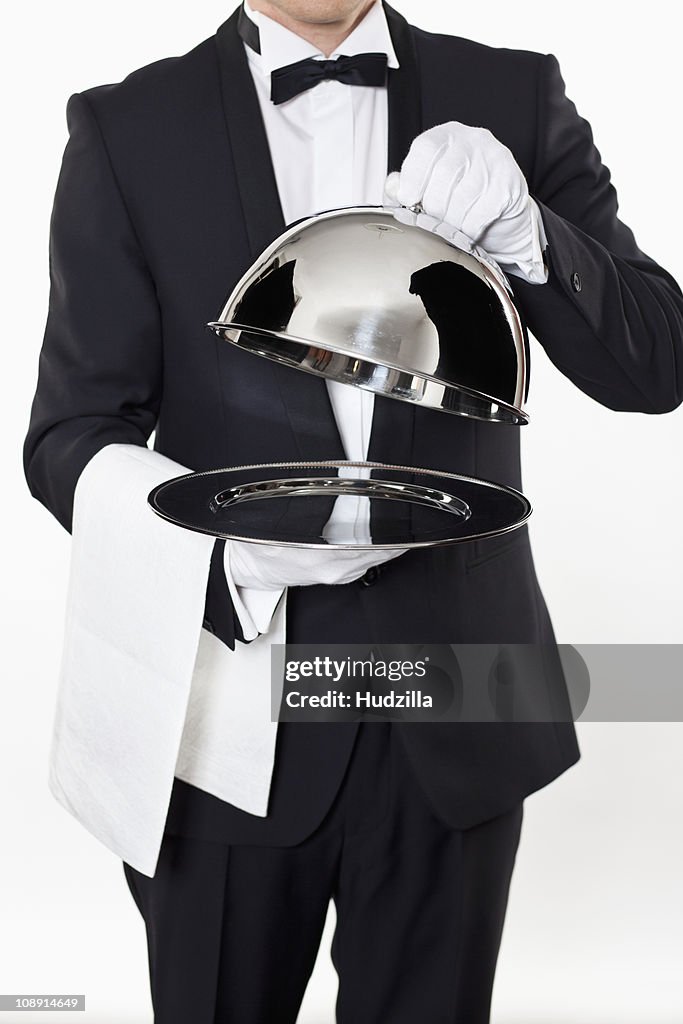 A butler taking the domed lid off an empty silver tray