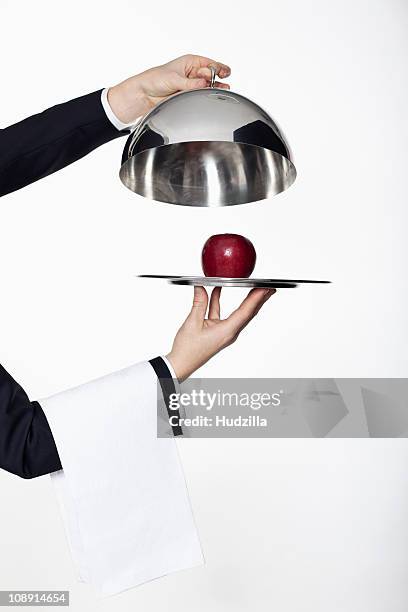 a butler taking the lid off a domed tray, revealing a red apple, focus on hands - cloche argent photos et images de collection