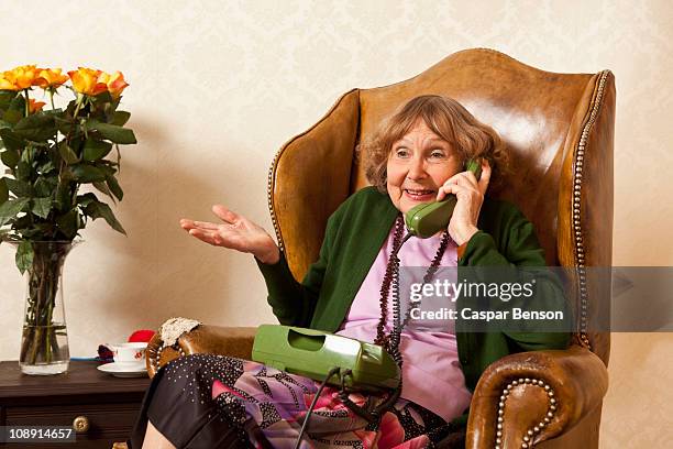 a senior woman talking on the phone in her living room - schulterzucken stock-fotos und bilder