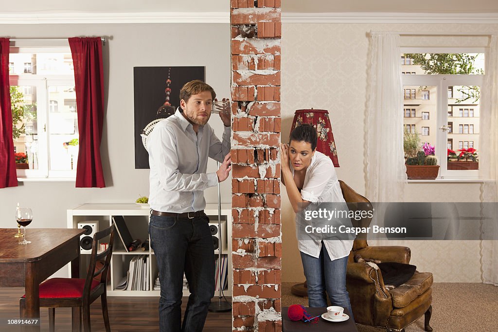 Man and woman listening on either side of wall with drinking glasses