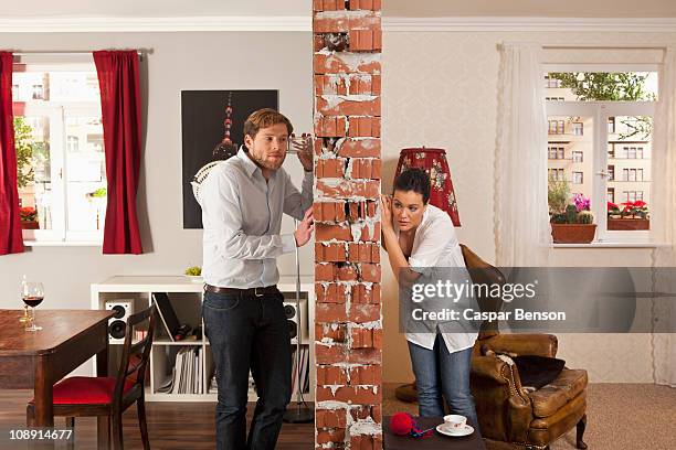 man and woman listening on either side of wall with drinking glasses - lauschen stock-fotos und bilder