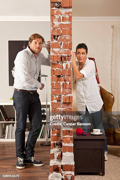 man and woman listening on either side of wall with drinking glasses - espiar una conversación fotografías e imágenes de stock