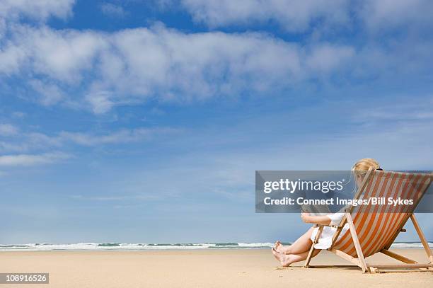 woman in deck chair on beach - beach deck chairs stock-fotos und bilder