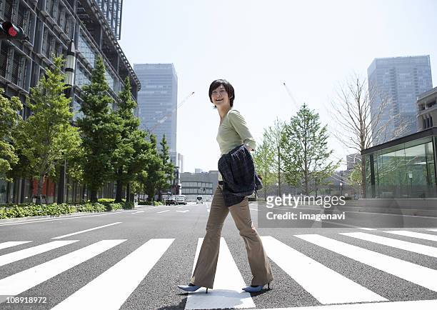 young woman crossing at crosswalk - marunouchi stock-fotos und bilder