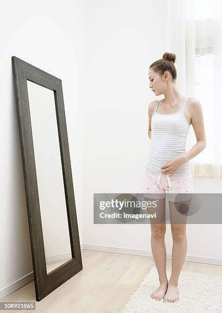 a young woman looking in a mirror - full length mirror fotografías e imágenes de stock