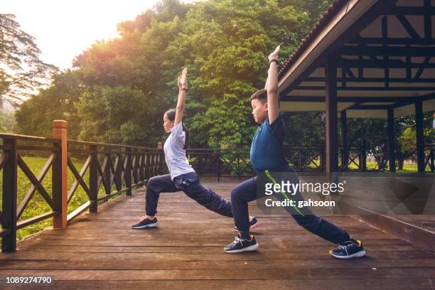 young asian athletic brother and sister doing exercise stretching and practicing yoga warrior pose in nature outdoor park morning. wearing sports outfit. concept of healthy lifestyle, training workout - yoga teen stock pictures, royalty-free photos & images