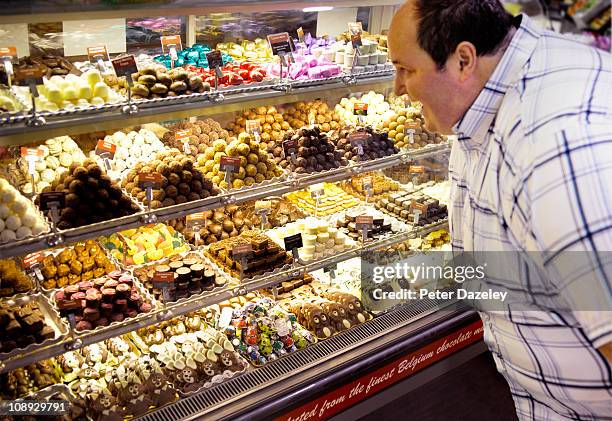 obese man looking at belgium chocolates - snoepwinkel stockfoto's en -beelden