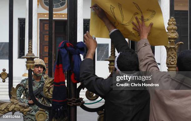 Anti-government protesters attach a sign to the gate of the Egyptian Parliament building as an Egyptian Army soldier guards inside on February 9,...