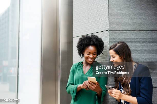 two women sharing with smart phones - friendly business phonecall stock pictures, royalty-free photos & images