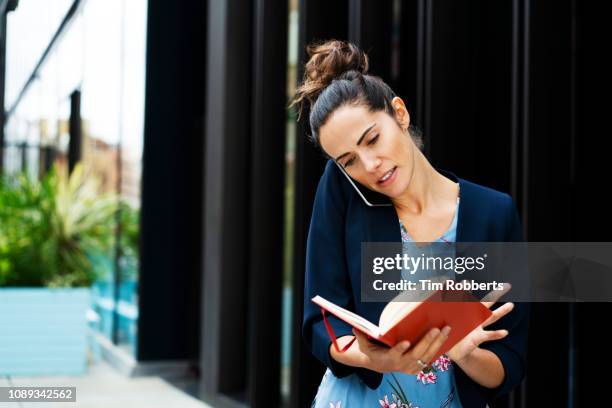 woman talking on smart phone looking at notebook - busy schedule stock pictures, royalty-free photos & images