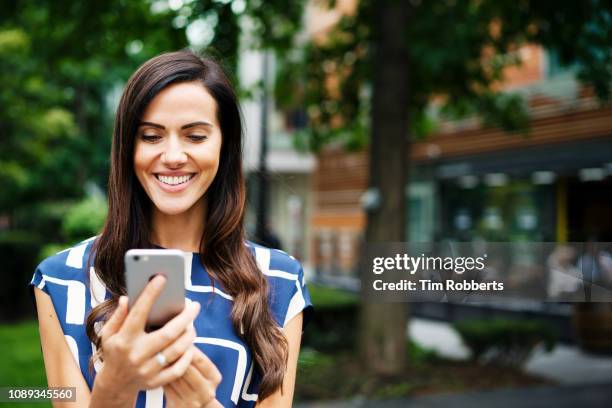 woman with smart phone, smiling - the city stock-fotos und bilder