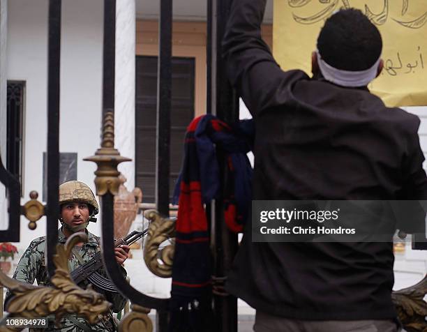 An anti-government protester attachs a sign to the gate of the Egyptian Parliament building while an Egyptian Army soldier watches from inside...