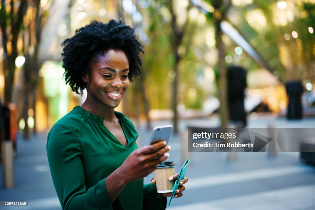 Woman using smart phone, holding coffee, smiling