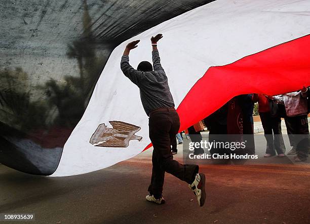 An anti-government protester runs under a large Egyptian flag in front of the Egyptian Parliament building Feburary 9, 2011 in Cairo, Egypt....