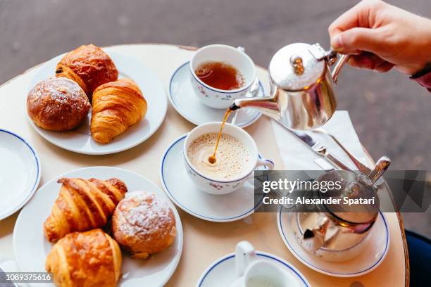 pouring tea in the cup while having breakfast at sidewalk cafe - croissant café stock-fotos und bilder