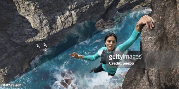 free climber hangs one handed on sea cliff rock face - hanging stock pictures, royalty-free photos & images