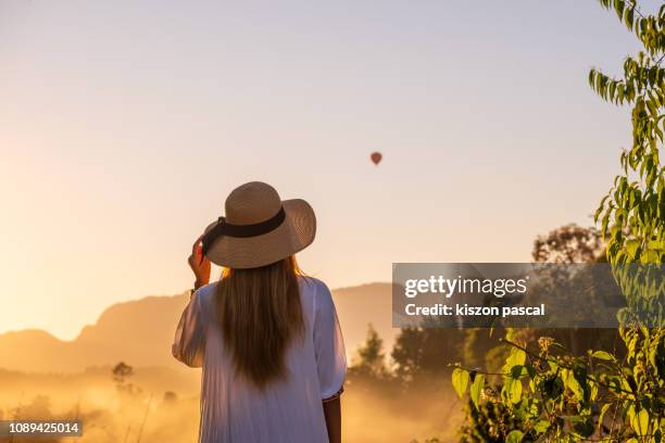 woman looking at hot air balloon in laos during foggy sunset . - vang vieng balloon stockfoto's en -beelden