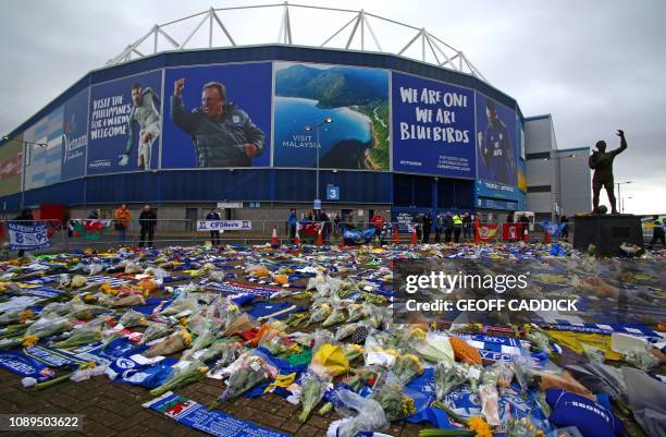 Man adds a Wales scarf to the display of Cardiff City scarves and jerseys, flowers, messages and other tributes to the football club's new signing...