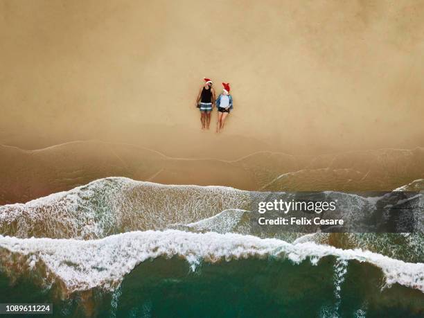 an aerial shot of a young couple sitting on the beach with a santa hat - christmas australia stock-fotos und bilder