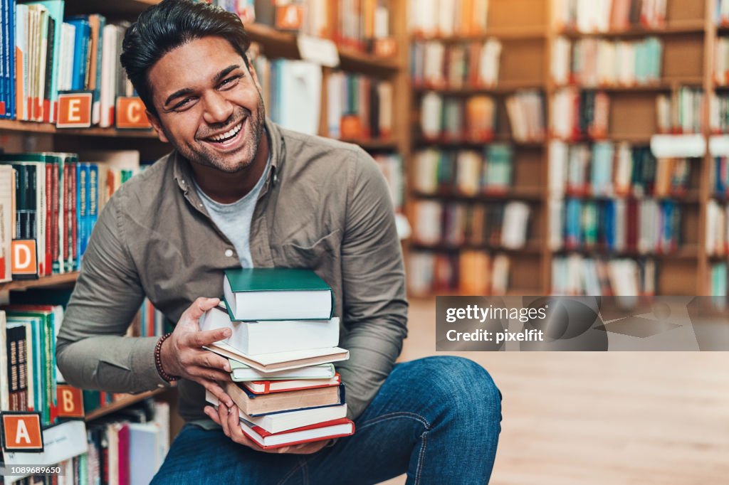 Happy young man with a pile of books in a bookstore