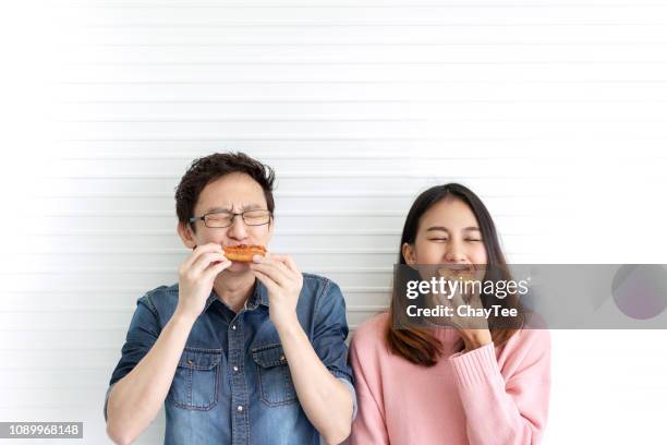 Attractive asian hungry couple eating pizza or fast food with smile and tasty facial expression on face with white wall background. Millennial lifestyle with friends concept. Man and woman enjoy meal.