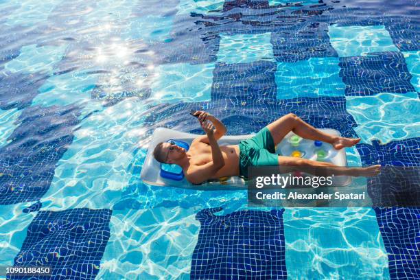 young man relaxing in the swimming pool on inflatable pool raft and using mobile phone - man in swimming pool stockfoto's en -beelden