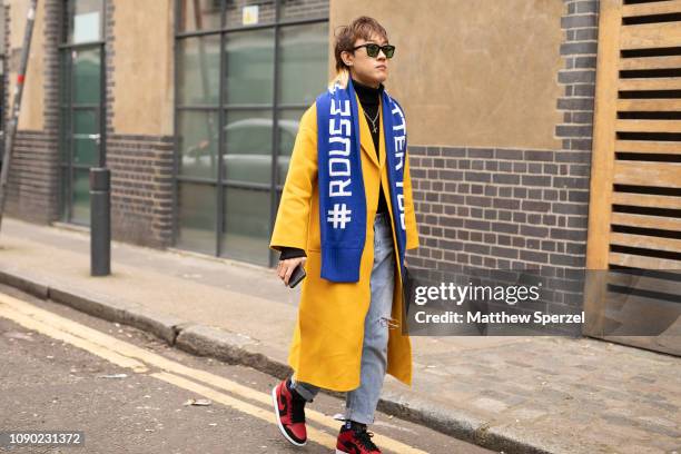 Guest is seen on the street wearing yellow coat, blue football scarf, red/black sneakers, blue jeans and sunglasses during London Fashion Week Men's...