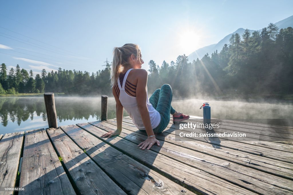 Jogging mujer relajante en muelle de lago en frescura disfrutando del sol de la naturaleza