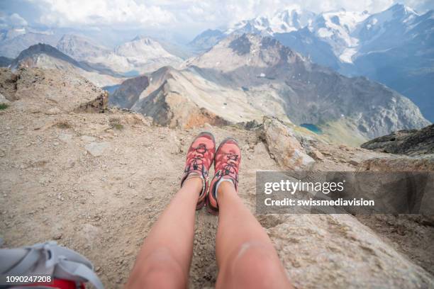 personal perspective of woman sit-in gon mountain peak looking down at feet and spectacular mountain range landscape of the swiss alps. people travel exploration discovery and achievement concept - pov shoes stock pictures, royalty-free photos & images