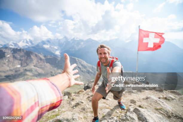 excursionista ayudando a su compañero de equipo en la cima de la montaña dando una mano para llegar a la cumbre, suiza - swiss flag fotografías e imágenes de stock