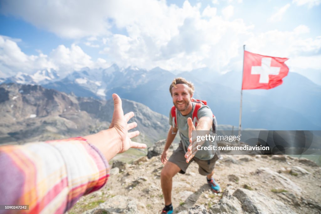 Hiker assisting teammate at mountain top giving a helping hand to reach summit, Switzerland
