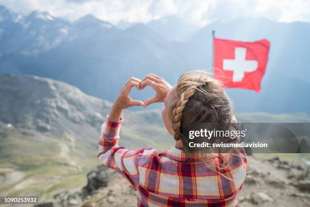 young woman making heart shape finger frame on mountain top overlooking the swiss alps; swiss flag - graubunden canton stock pictures, royalty-free photos & images