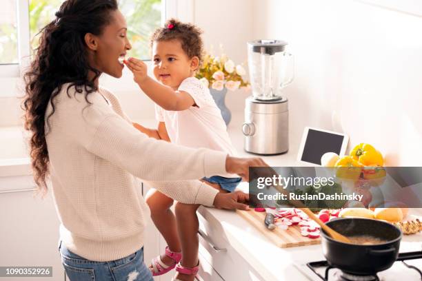 daughter child feeding mother while the mum cooking. - taste test stock pictures, royalty-free photos & images