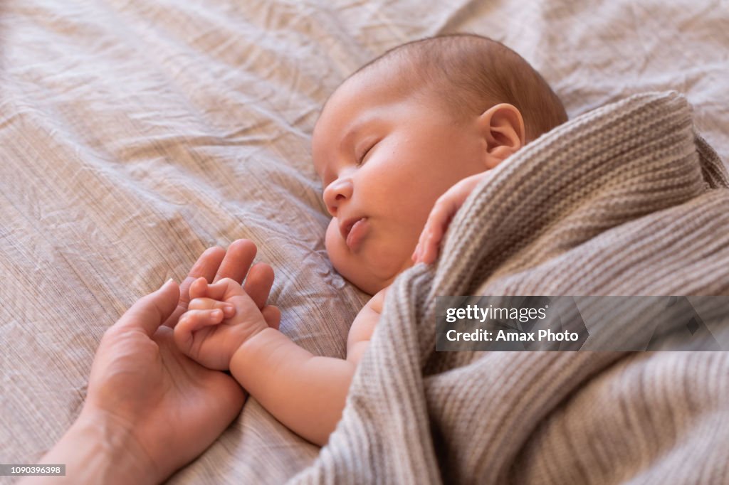 Close-up of sleeping baby hand in the mother's hand on the bed. New family and baby sleep concept