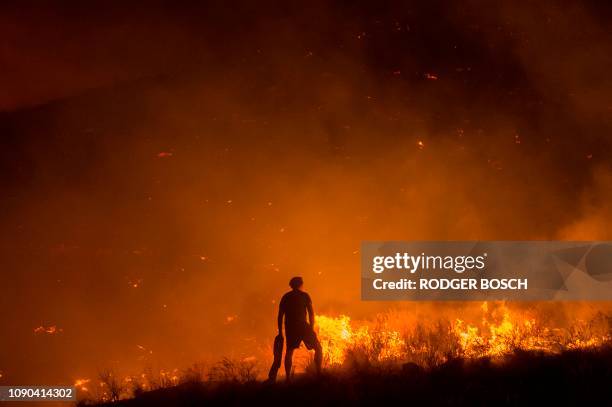 Local resident using a wet towel looks on as he fights one front of a large brush fire that started around the mountains in the city centre on...