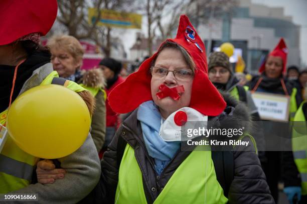 Female Gilets Jaunes or Yellow Vest protestor wearing a symbolic red bonnet of the French Republique, marches with her mouth taped shut at Place de...