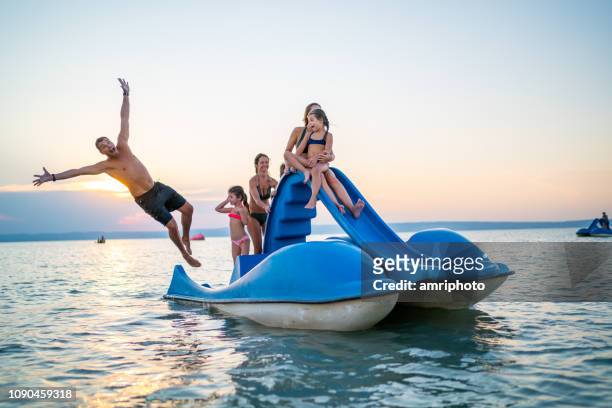 famiglia felice godendo tramonto estivo sul lago con pedalò - jumping of boat foto e immagini stock