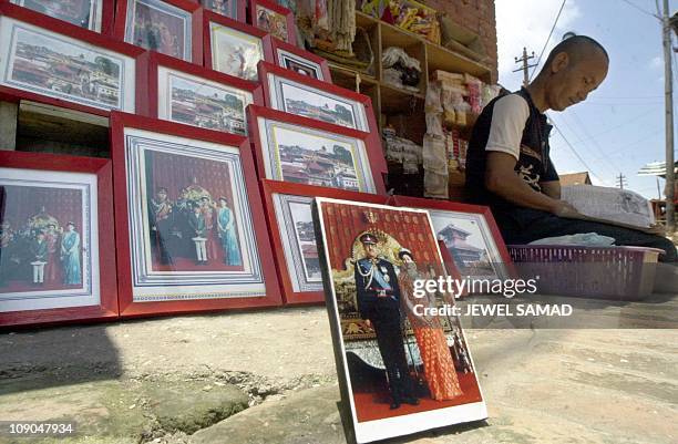 Nepalese street vendor reads a local newspaper, waiting for customers to buy photographs of the past royal family, in front of a temple in Kathmandu,...