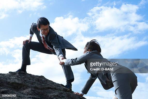 businessman helping woman on the cliff - businessman challenge stock-fotos und bilder