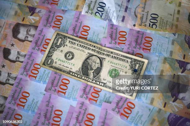 This ilustration shows Venezuelan Bolivar banknotes and a US one-dollar bill in Caracas on January 28, 2019. - Venezuela devalued its currency by...