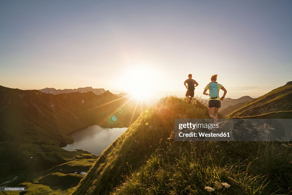 Germany, Allgaeu Alps, man and woman running on mountain trail