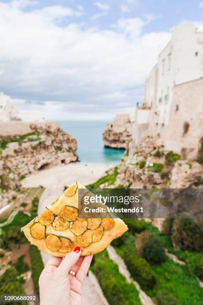 italy, puglia, polognano a mare, woman's hand holding piece of zucchini focaccia - puglia italy stock pictures, royalty-free photos & images