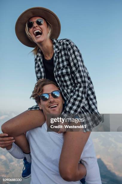 happy young man carrying girlfriend piggyback - fun sommer berge stock-fotos und bilder