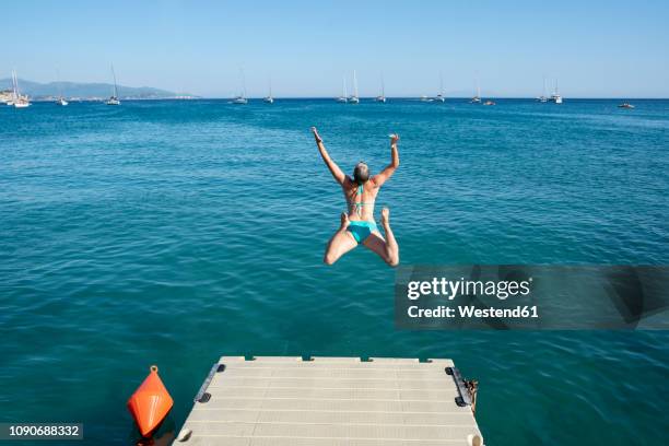 greece, parga, carefree woman jumping from jetty into the sea - bathing jetty stock pictures, royalty-free photos & images